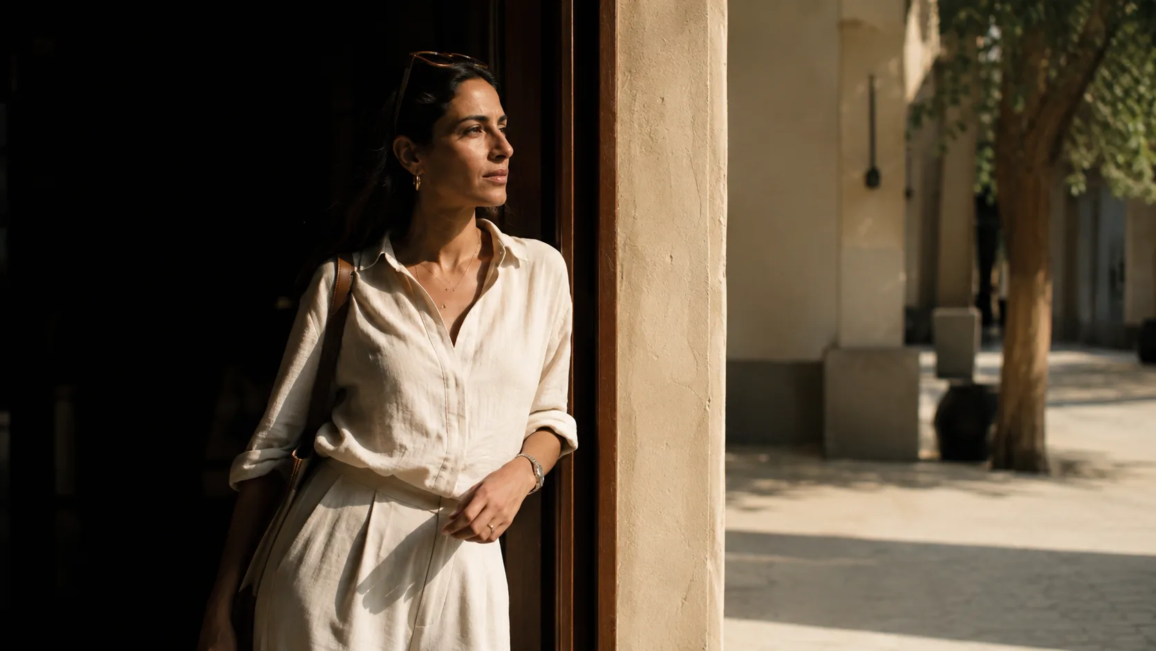 A woman steps out of a shaded doorway into hard summer sunlight on a Dubai street